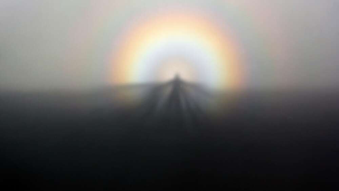 A brocken spirit cast on the mist, with a rainbow in the background.
